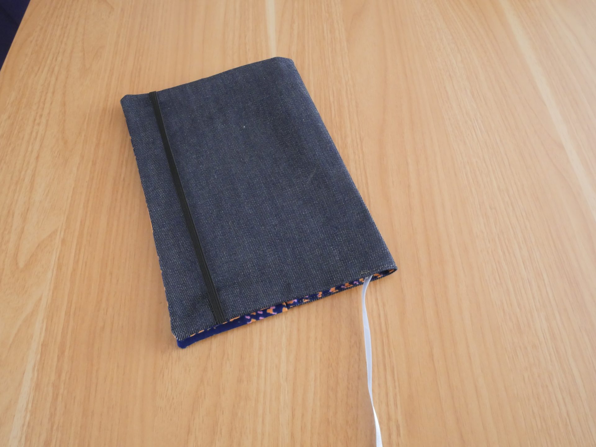 Dos du couvre-livre ratonetpanda en jean brut avec élastique noir de fermeture et liseré wax coloré