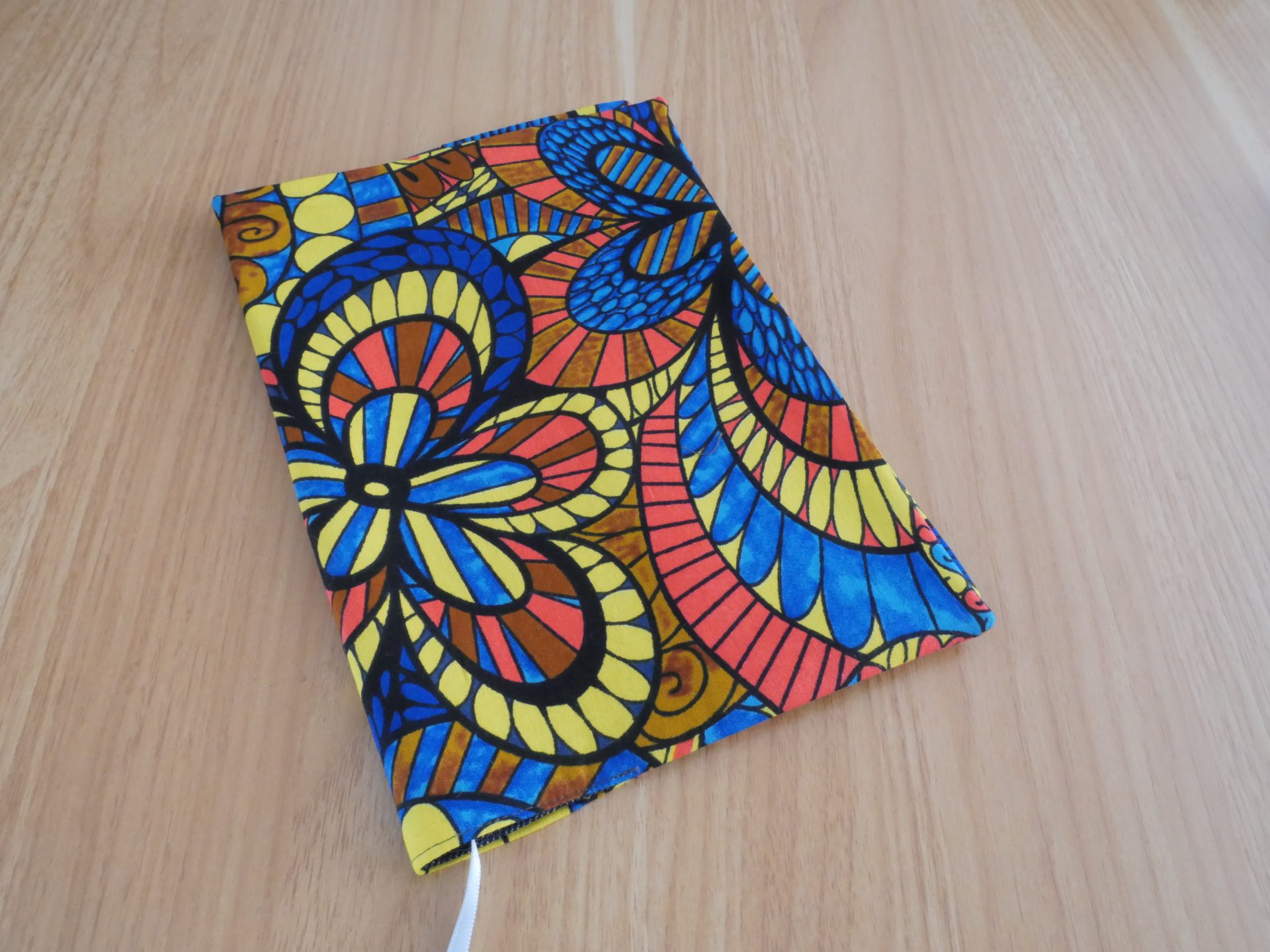 Couvre-livre fait main en tissu wax africain coloré, ouvert, avec doublure jean gris, marque-page satin blanc et poche intérieure