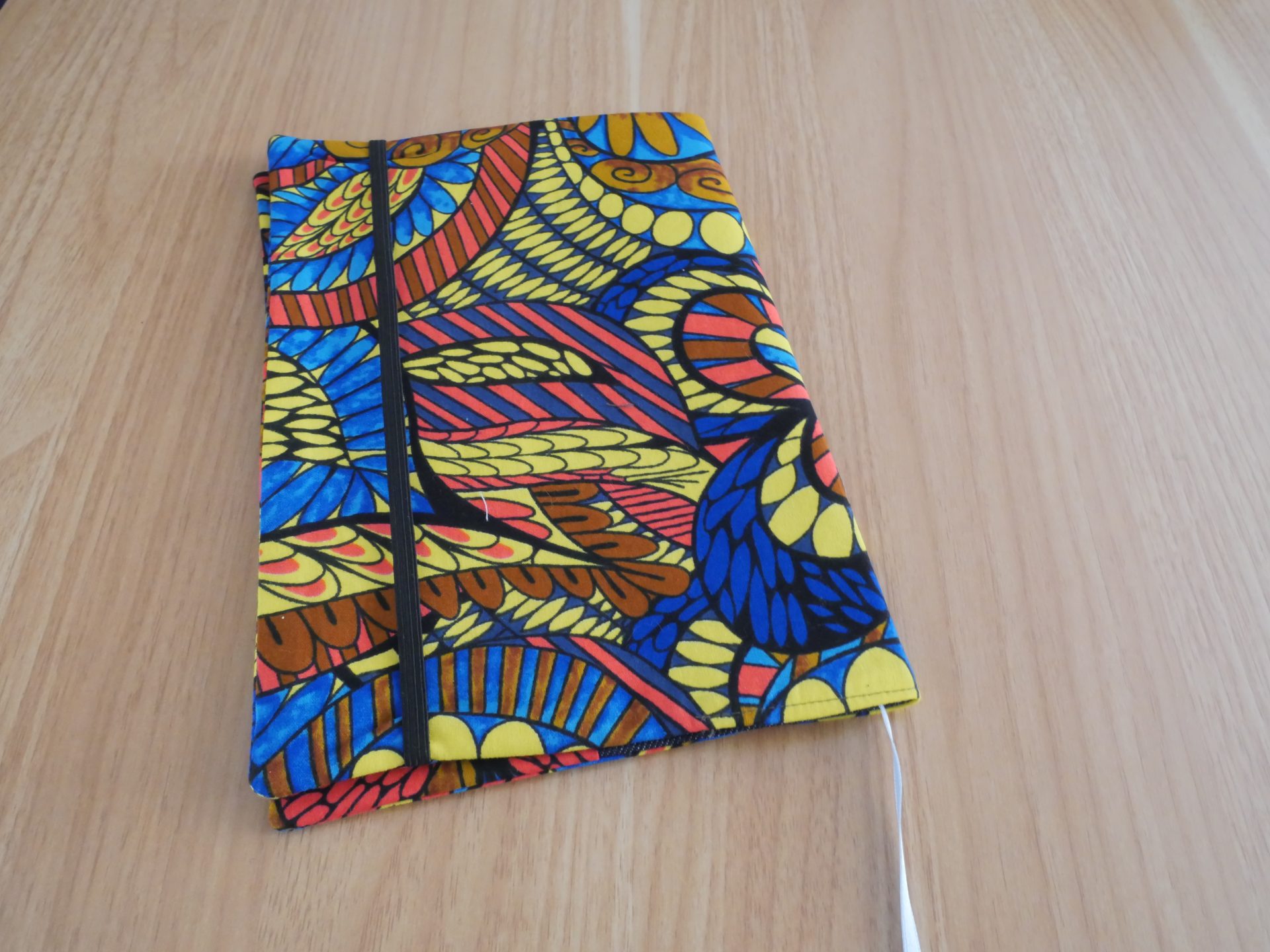 Couvre-livre fait main en tissu wax africain coloré, ouvert, avec doublure jean gris, marque-page satin blanc et poche intérieure