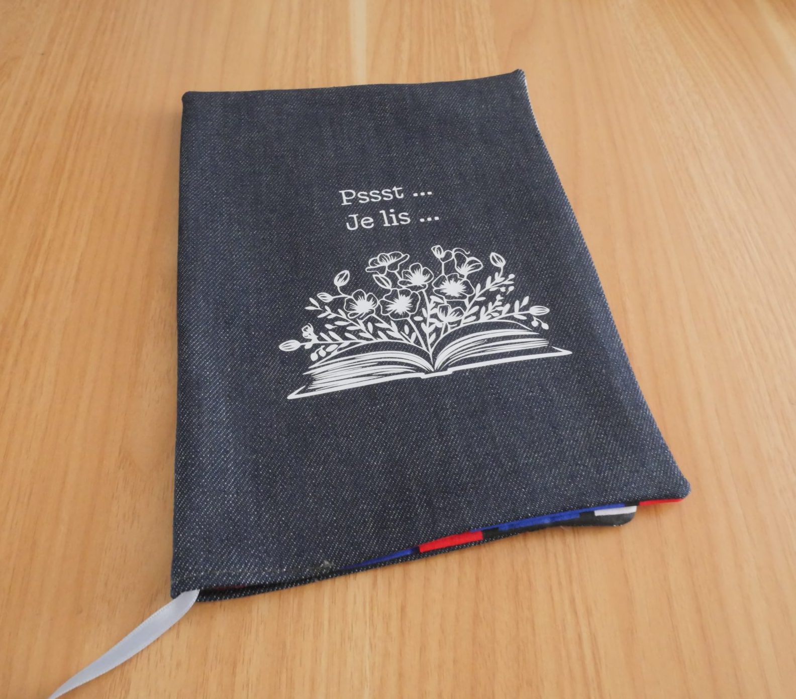 Couvre-livre fait main en jean brut avec sérigraphie blanche "Pssst Je lis" et illustration livre fleuri, marque-page satin blanc